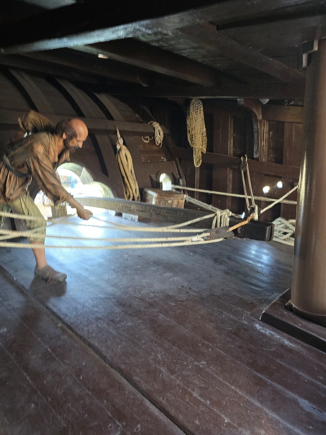 A crew mannequin demonstrating rigging work below deck on the ship replica